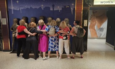 Las Vegas group of women taking a photo together at night in front of a cityscape mural.