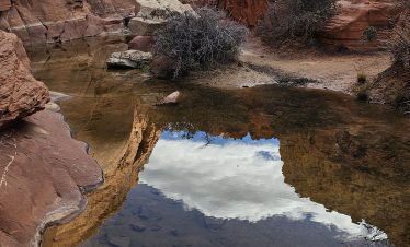 Hikers exploring the scenic Red Rock Canyon with rugged cliffs and a reflective water pool.