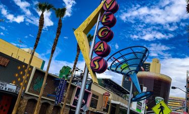 Fremont Street Experience sign in downtown Las Vegas with palm trees and blue sky.