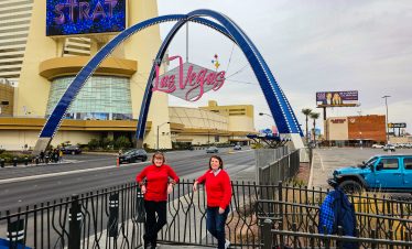 Two women in red shirts pose in front of Las Vegas Strip sign at Fremont Street.