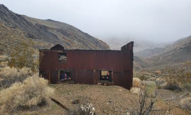 Rusty abandoned building in Death Valley with mountains in the background.
