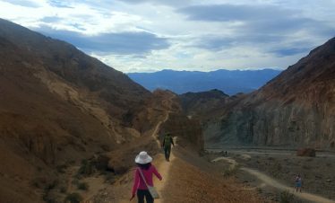 Hikers exploring a scenic trail in Death Valley with mountains and blue sky.