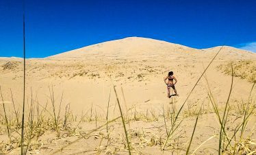 Hiker walking on sand dunes in Death Valley under a clear blue sky.
