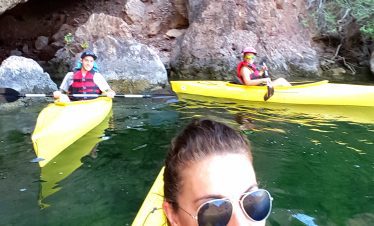 Group kayaking adventure on a calm river with rocky cliffs in the background.