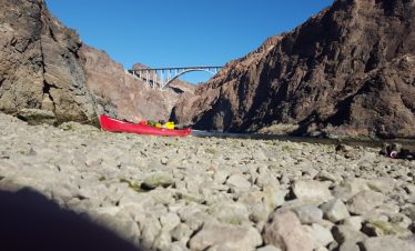 Red kayak on rocky shore with canyon and bridge in background.
