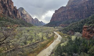 Stunning view of Zion Canyon with river and cliffs under cloudy sky.