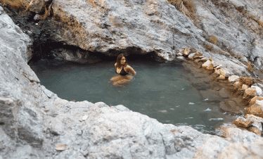 Woman relaxing in a natural hot spring surrounded by rocky terrain.