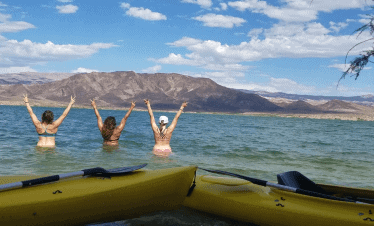 Three kayakers in Black Canyon with mountains and blue sky in background.